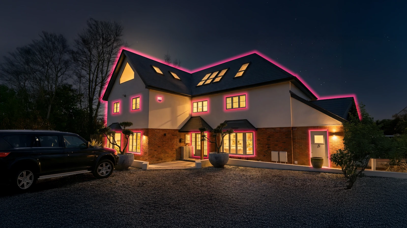 A two-story house at night with illuminated windows and pink lights outlining the roof.